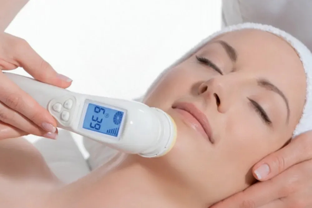 Woman receiving a facial treatment with a handheld device displaying temperature, highlighting professional skincare services at The Beauty Haven.