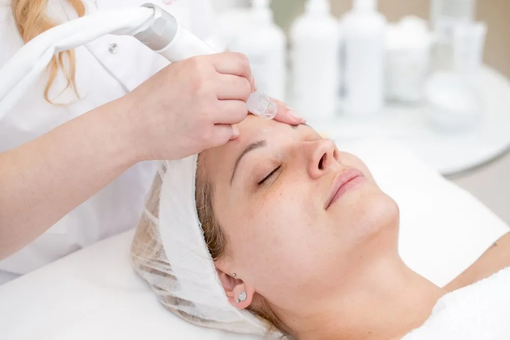 Woman receiving a skin rejuvenation treatment, facial care procedure with a handheld device, in a beauty clinic setting, surrounded by skincare products, highlighting anti-ageing solutions in Liverpool, NSW.