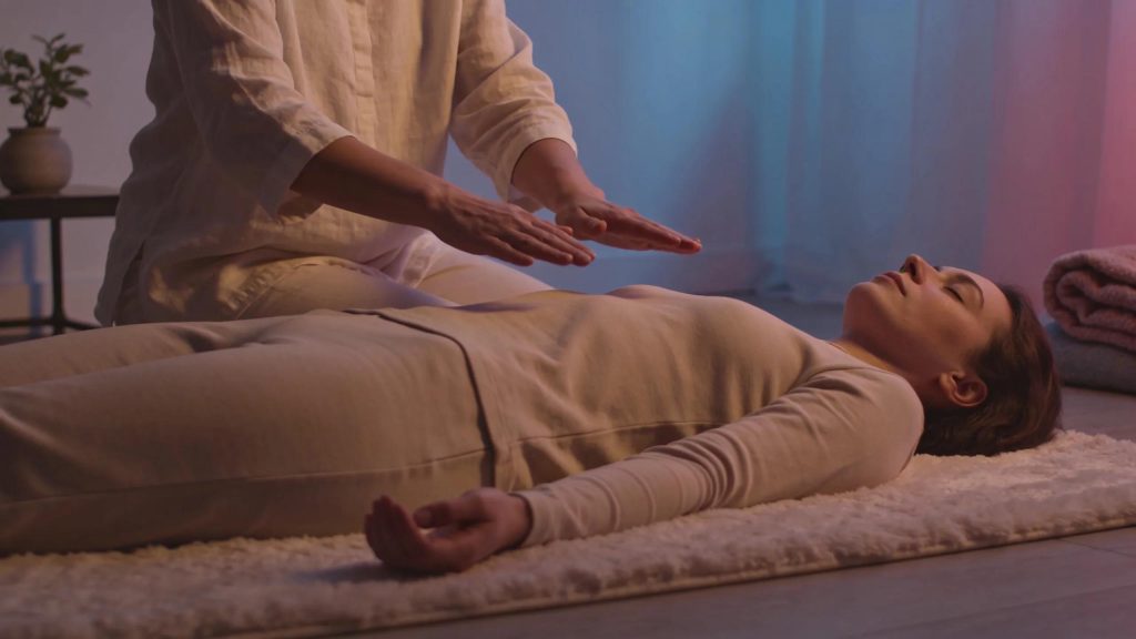 Reiki practitioner channeling energy over relaxed client during healing session.