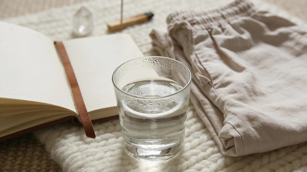 Glass of water, notebook, and soft blanket illustrating Reiki healing preparation.